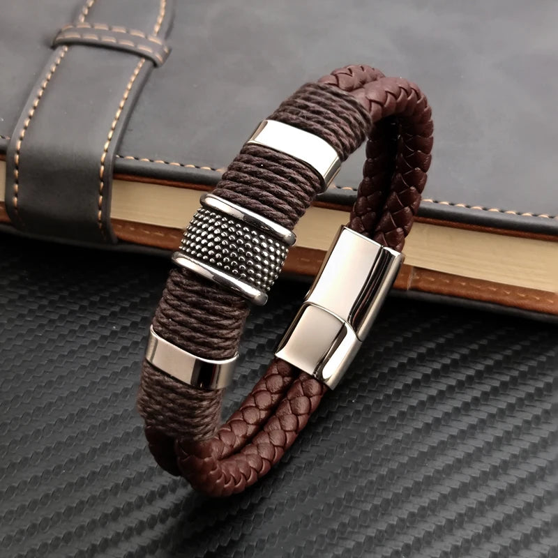 Brown braided leather bracelet with silver metal clasps on a textured surface
