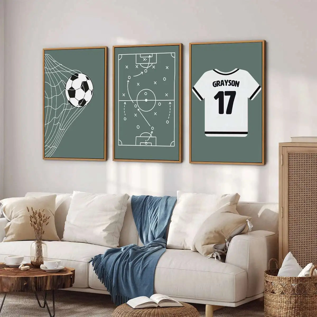 Three framed wall art prints with soccer-themed designs hang above a white sofa in a styled living room. The left print shows a soccer ball inside a net on a muted green background, the center print shows a soccer tactic diagram, and the right print shows a white jersey with the name GRAYSON and number 17.