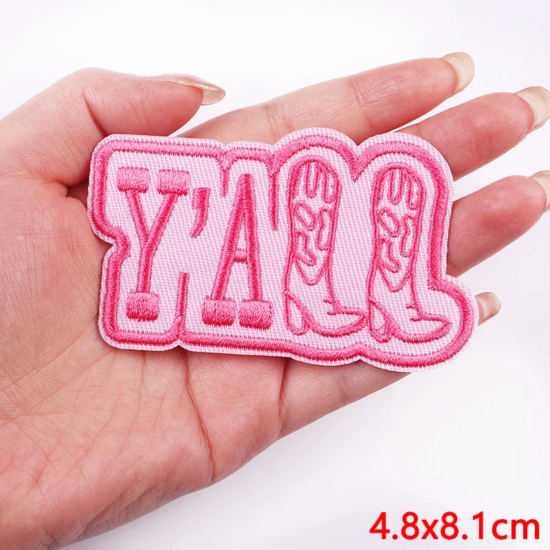 Pink embroidered patch with 'YAM' text and cowboy boot design held in a hand.