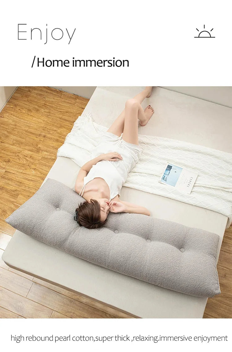 Person lying on a large gray pillow in a minimalistic room with wooden floor.