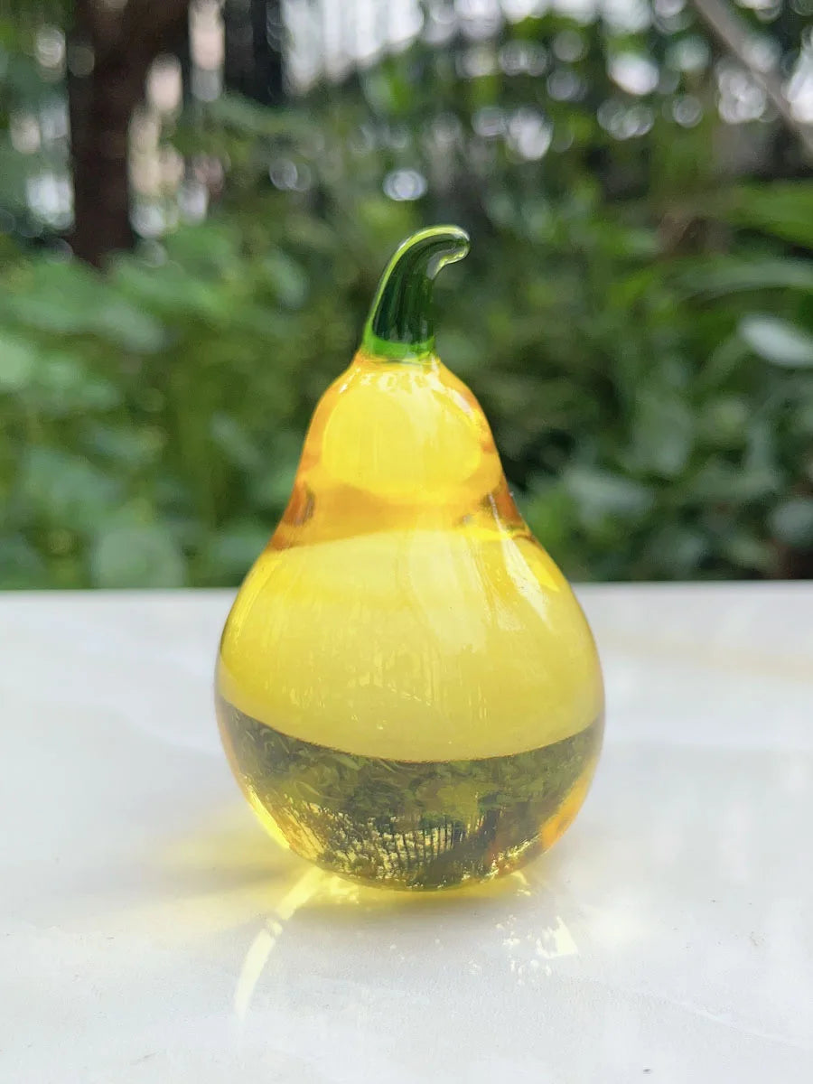Glass pear-shaped object on a white surface with a blurred green outdoor background