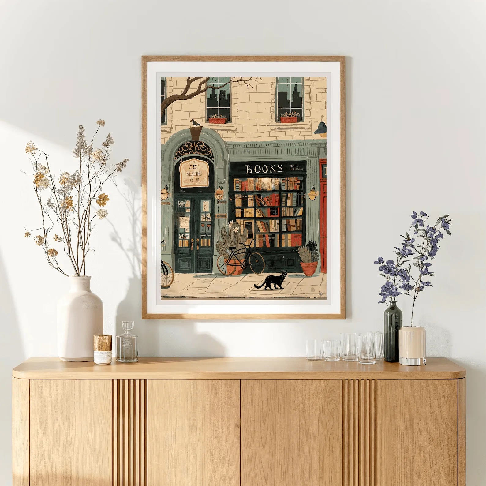 Framed artwork of a bookshop on a wall above a wooden cabinet.