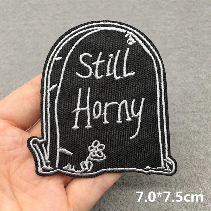 Embroidered patch with 'Still Horny' text held in a hand on a gray background