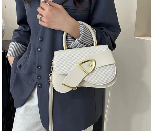 White handbag with gold accents held by a person wearing a dark blue outfit.