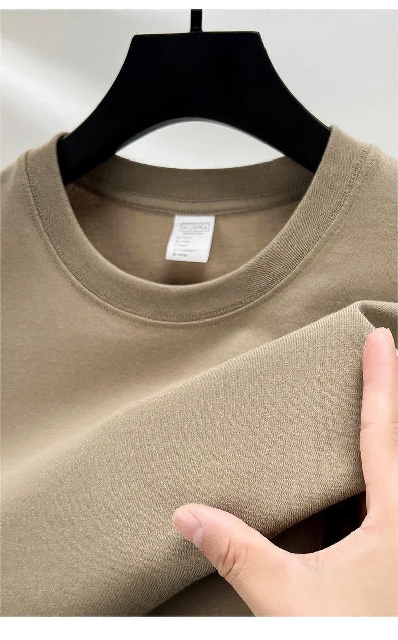 Beige t-shirt on a hanger with a hand touching the fabric, against a neutral background