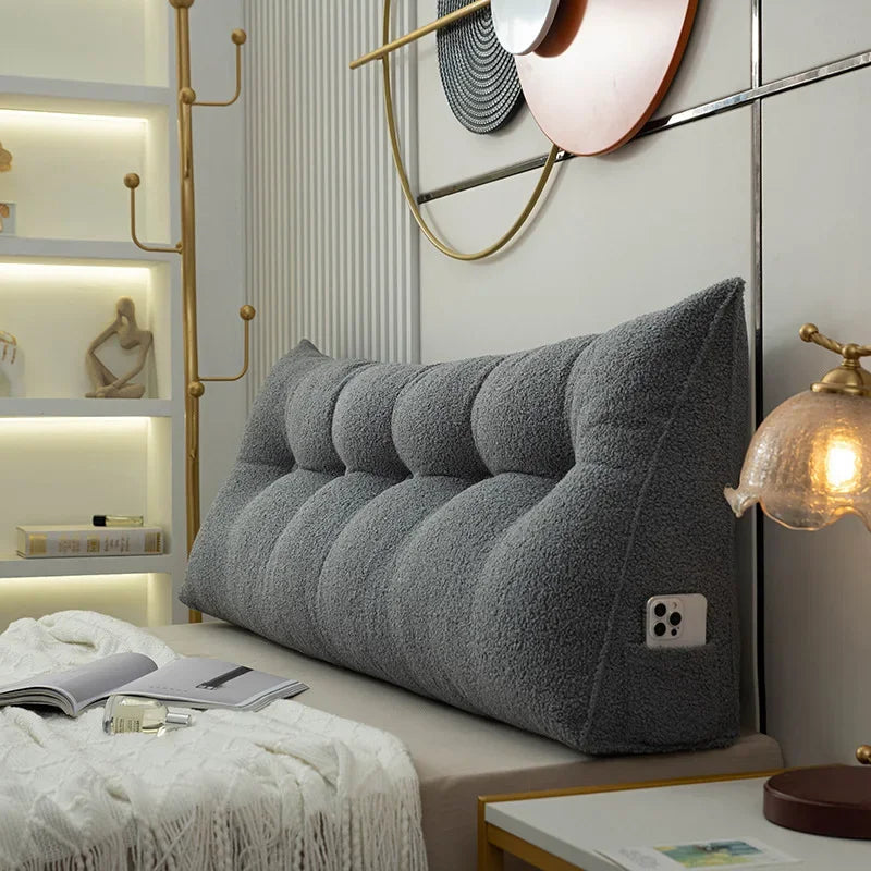 Gray wedge-shaped pillow on a bed in a stylish bedroom setting with lighting fixtures.