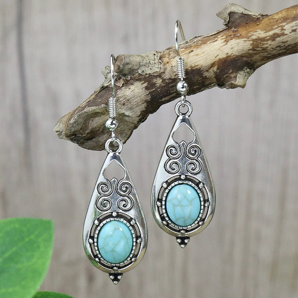Silver earrings with turquoise stones hanging on a branch.