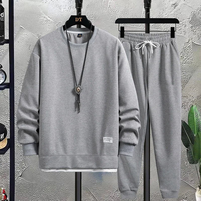 Gray sweatshirt and pants set on hangers against a textured wall.