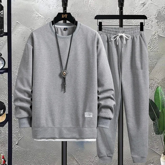 Gray sweatshirt and pants set on hangers against a textured wall.
