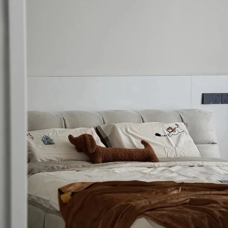 brown dachshund-shaped cushion on a Bed with pillows and a blanket in a bedroom setting