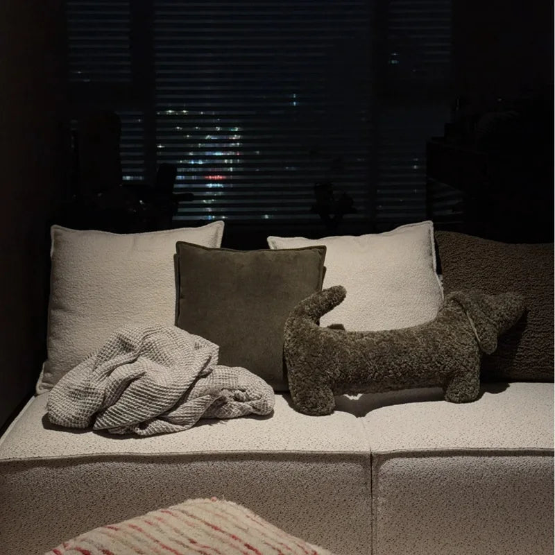 dachshund-shaped cushion on a Cozy seating area with pillows and a plush toy on a couch at night.