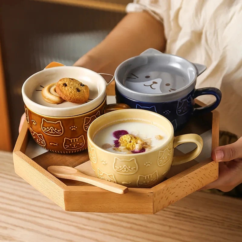 Three ceramic mugs with cat designs on a wooden tray, one containing a dessert.