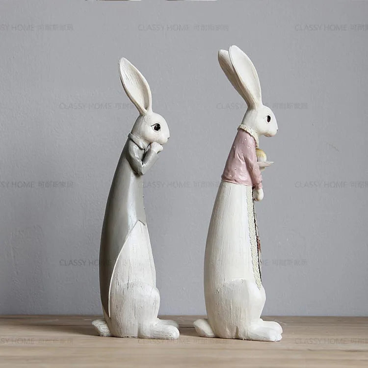 Two decorative rabbit figurines on a wooden surface with a gray background.