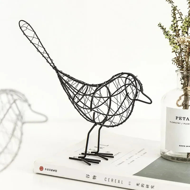 Black wire bird sculpture on a surface with a jar and paper in the background