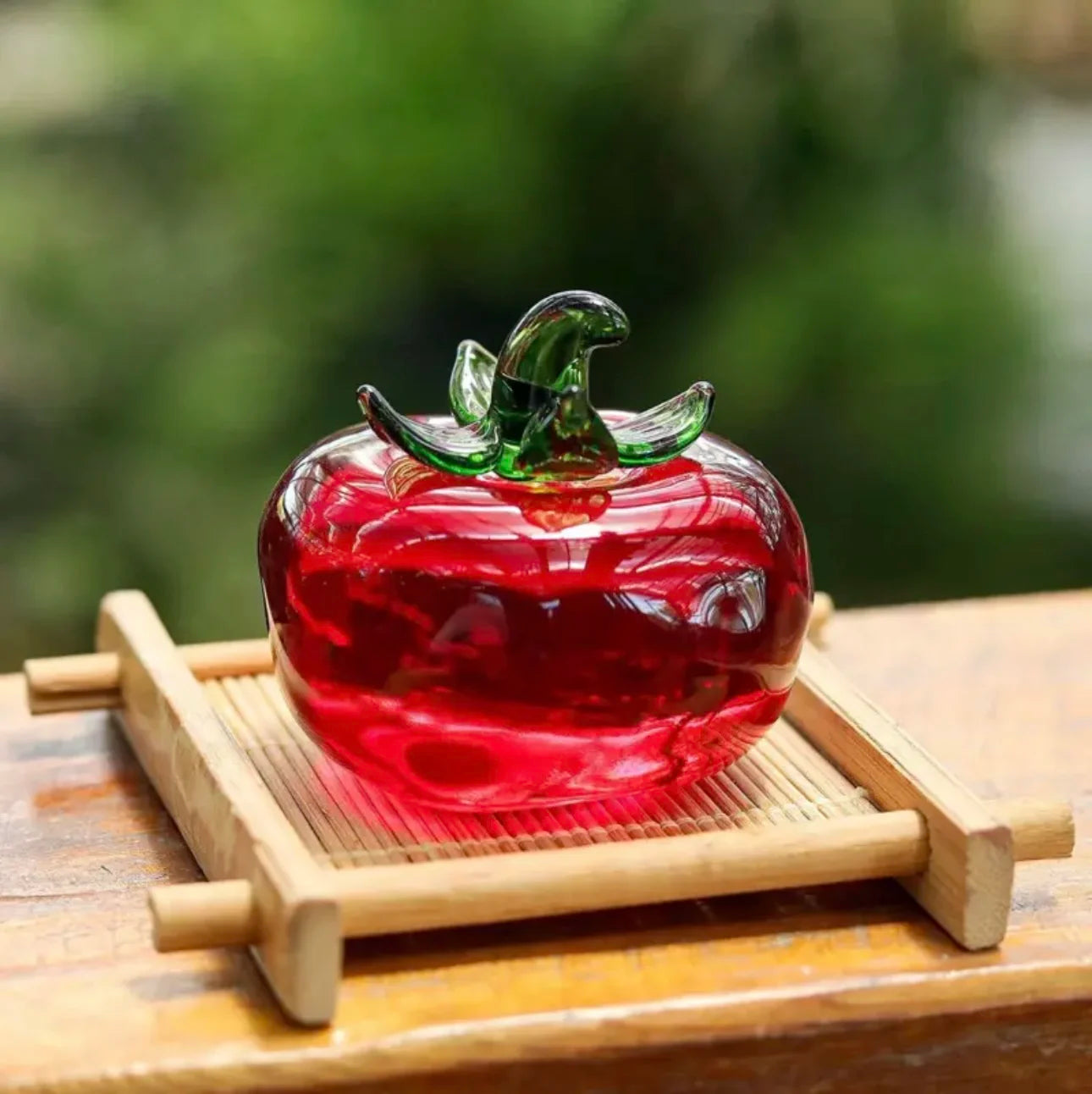 Glass apple sculpture on a wooden stand with a blurred green background