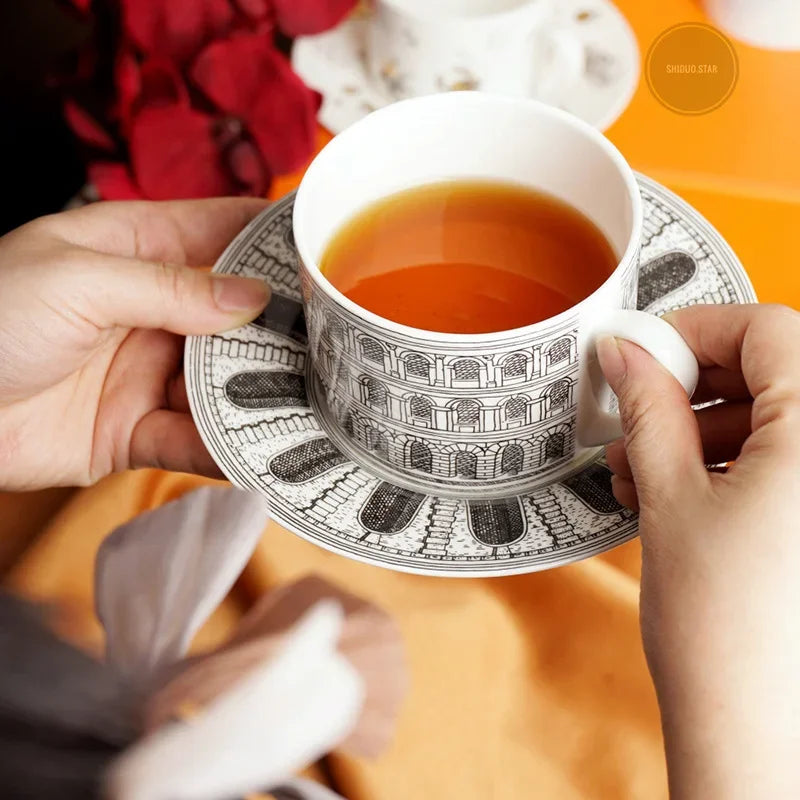 Person holding a decorative tea cup with a patterned saucer on an orange surface.