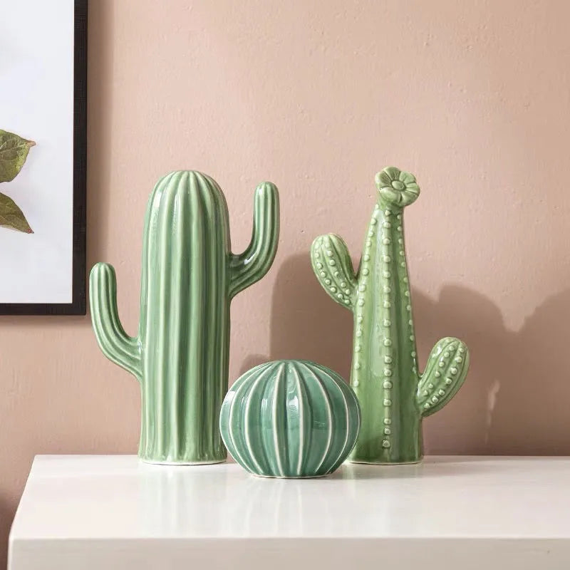 Three green cactus-shaped vases on a white surface with a pink wall background