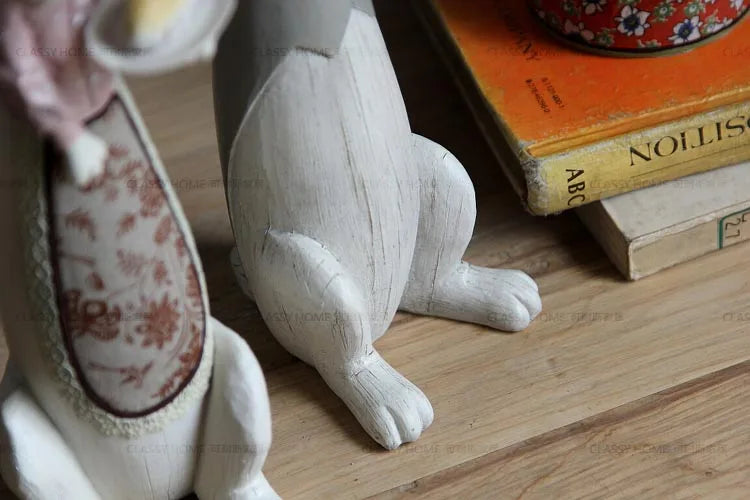 Small white rabbit figurine on a wooden surface with books and a decorative item in the background.