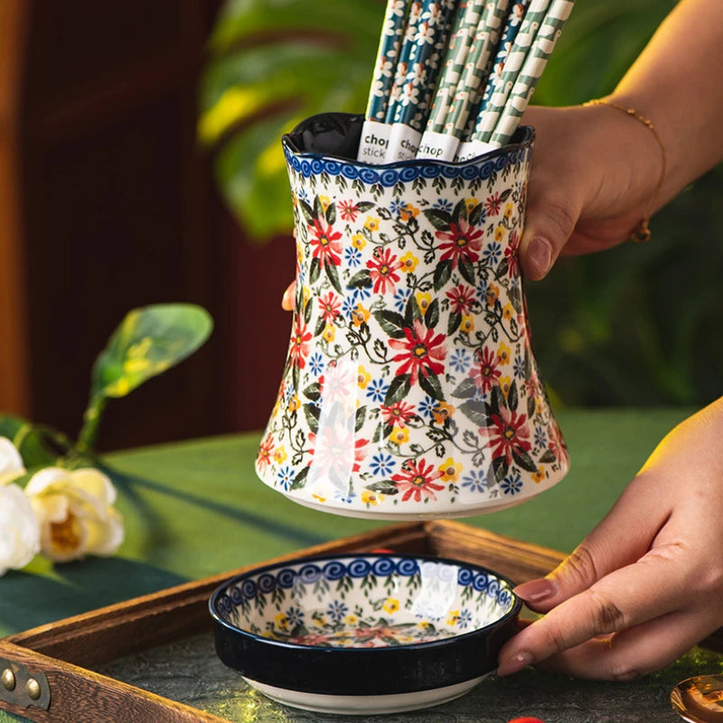 Decorative ceramic holder with floral design holding straws on a table with a bowl.