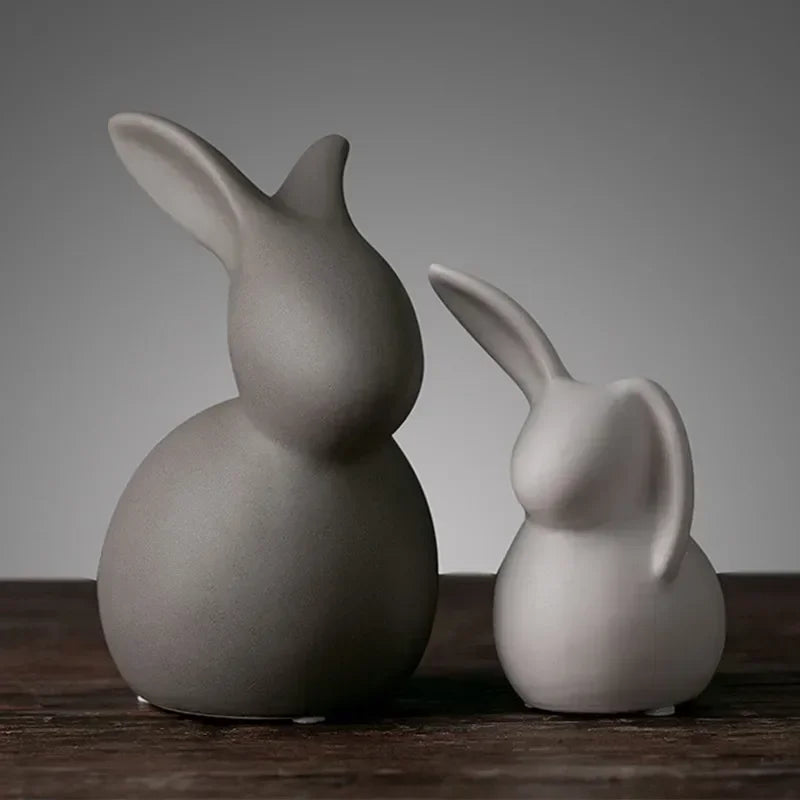 Two ceramic rabbit figures on a wooden surface with a neutral background