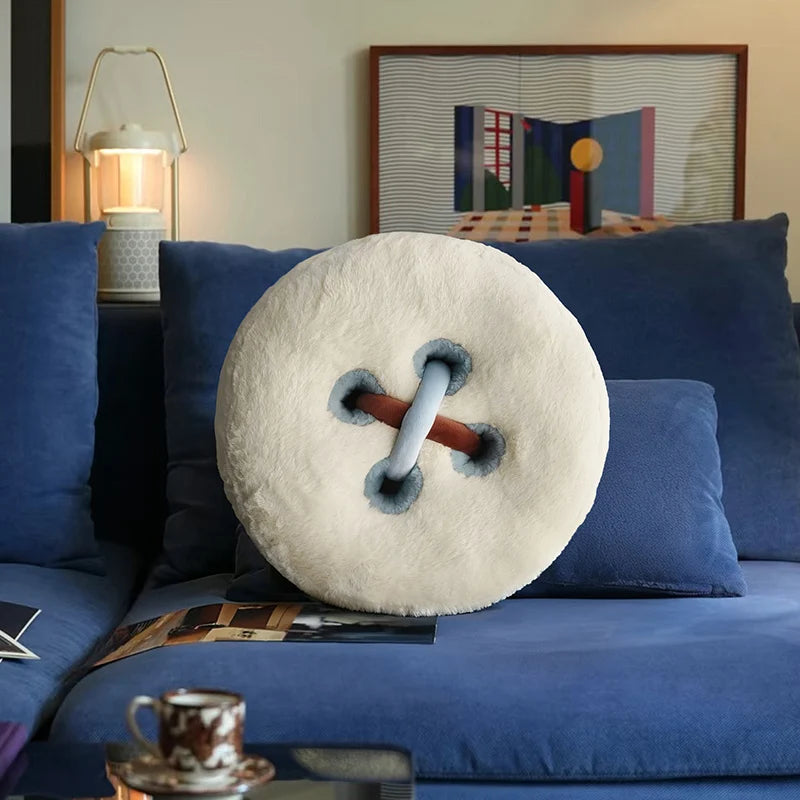 Round decorative pillow with a button design on a blue sofa in a living room.