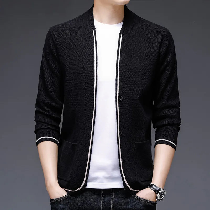 Person wearing a black cardigan over a white shirt on a gray background