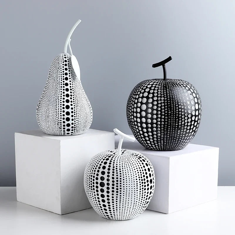 Decorative black and white sculptures of a pear, apple, and pumpkin on white cubes against a gray background.