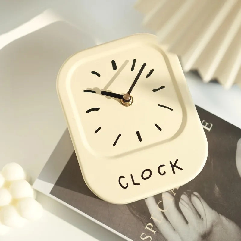 Small beige clock with 'CLOCK' text on a surface with a blurred background