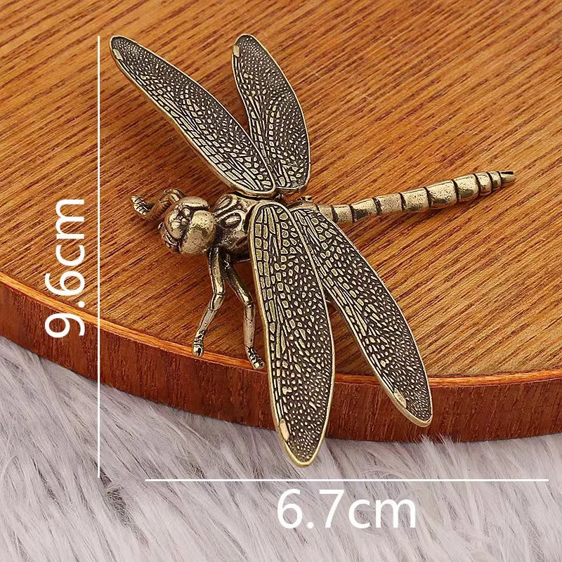 Bronze dragonfly-shaped object with measurements on a wooden surface