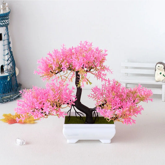 Artificial pink bonsai tree in a white pot on a light gray surface with decorative items in the background.