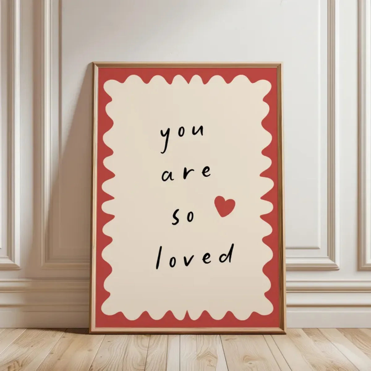 Framed artwork with 'you are so loved' text and a heart on a beige wall.