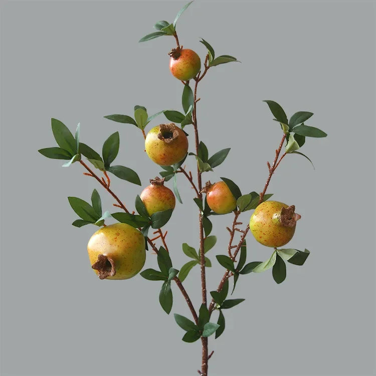 Artificial pomegranate branch with green leaves on a gray background