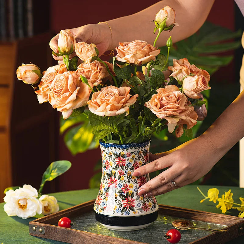Person holding a bouquet of peach-colored roses in a decorative vase on a table.