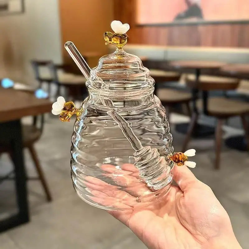Clear honeycomb-shaped glass drink container with a straw held in a hand, blurred restaurant interior in the background
