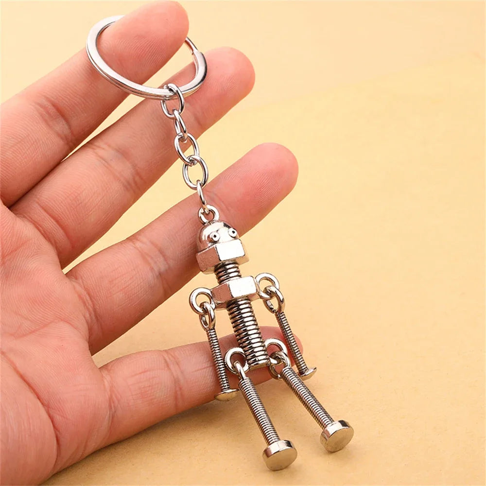 Metallic keychain shaped like a robot held by a hand against a yellow background