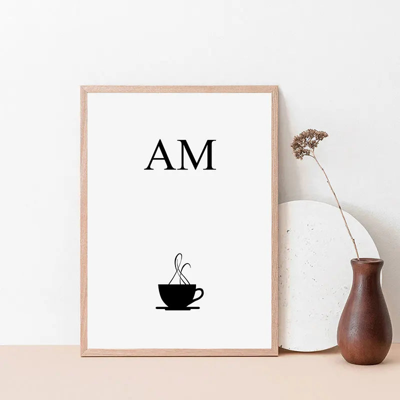Framed artwork with 'AM' and a coffee cup silhouette on a white background, placed on a surface with decorative items.