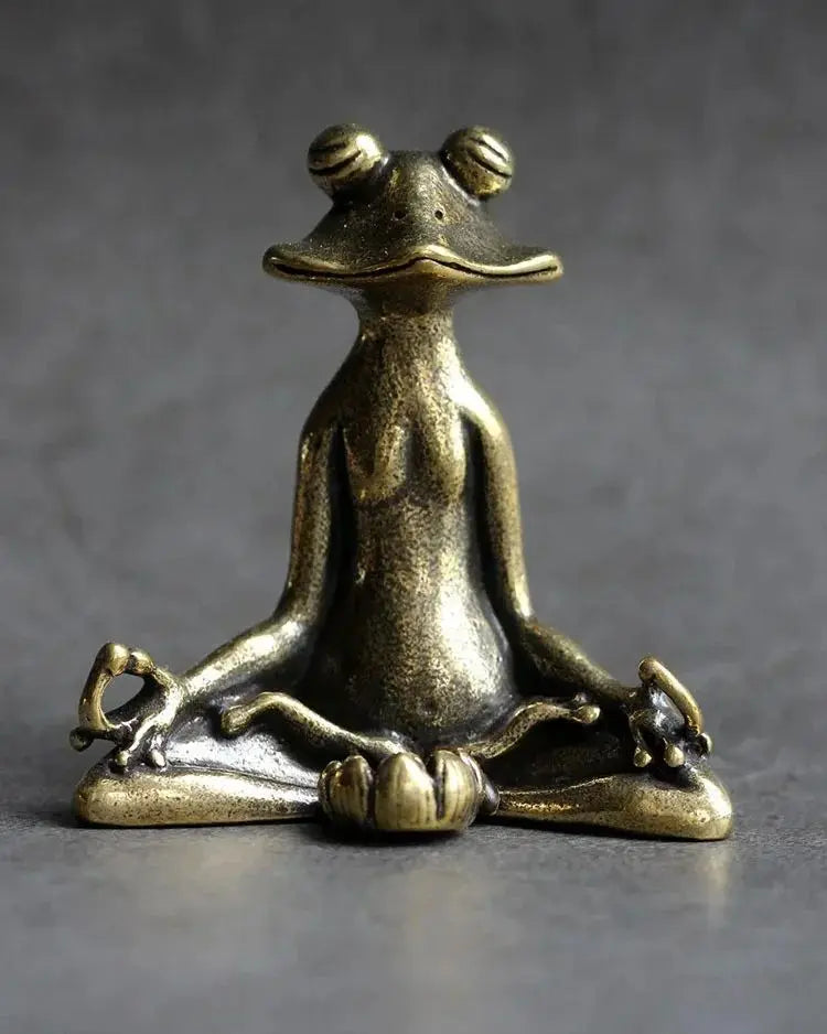 Bronze frog sculpture in a meditative pose on a gray background