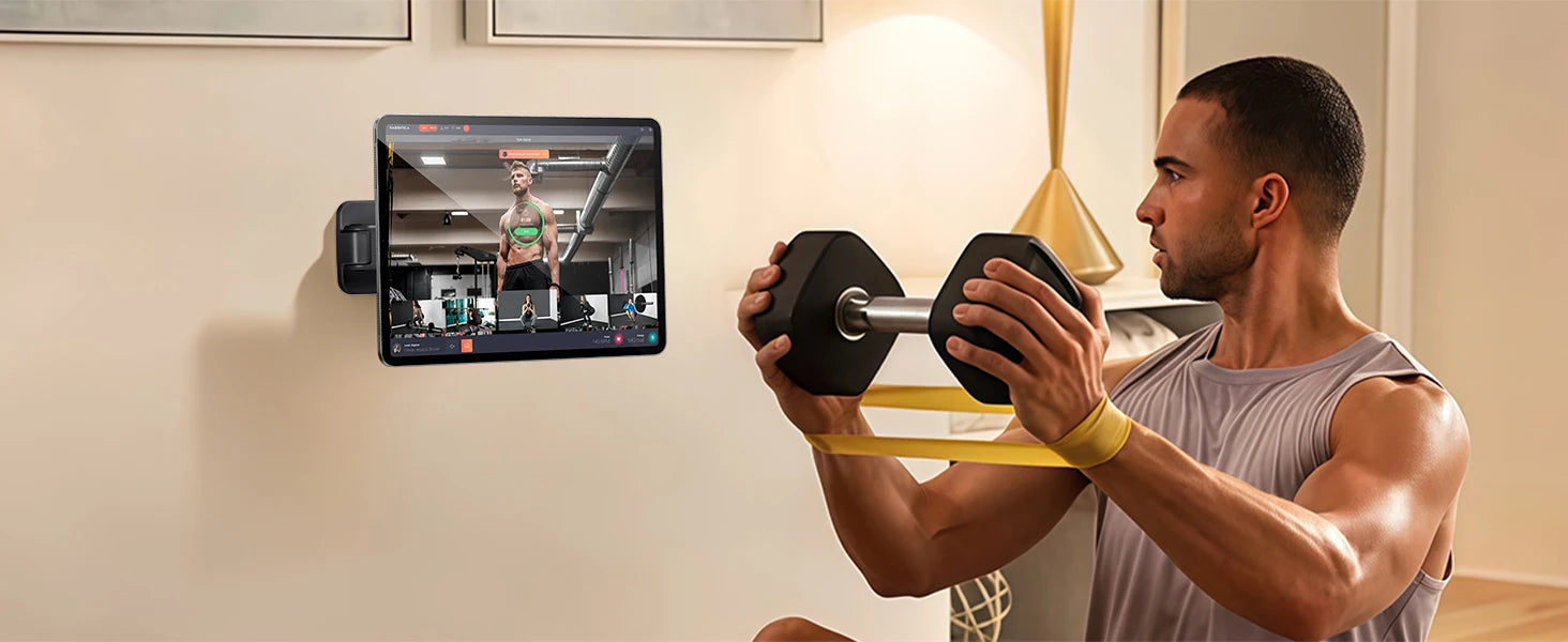 Man exercising with a dumbbell in front of a tablet displaying a workout video.