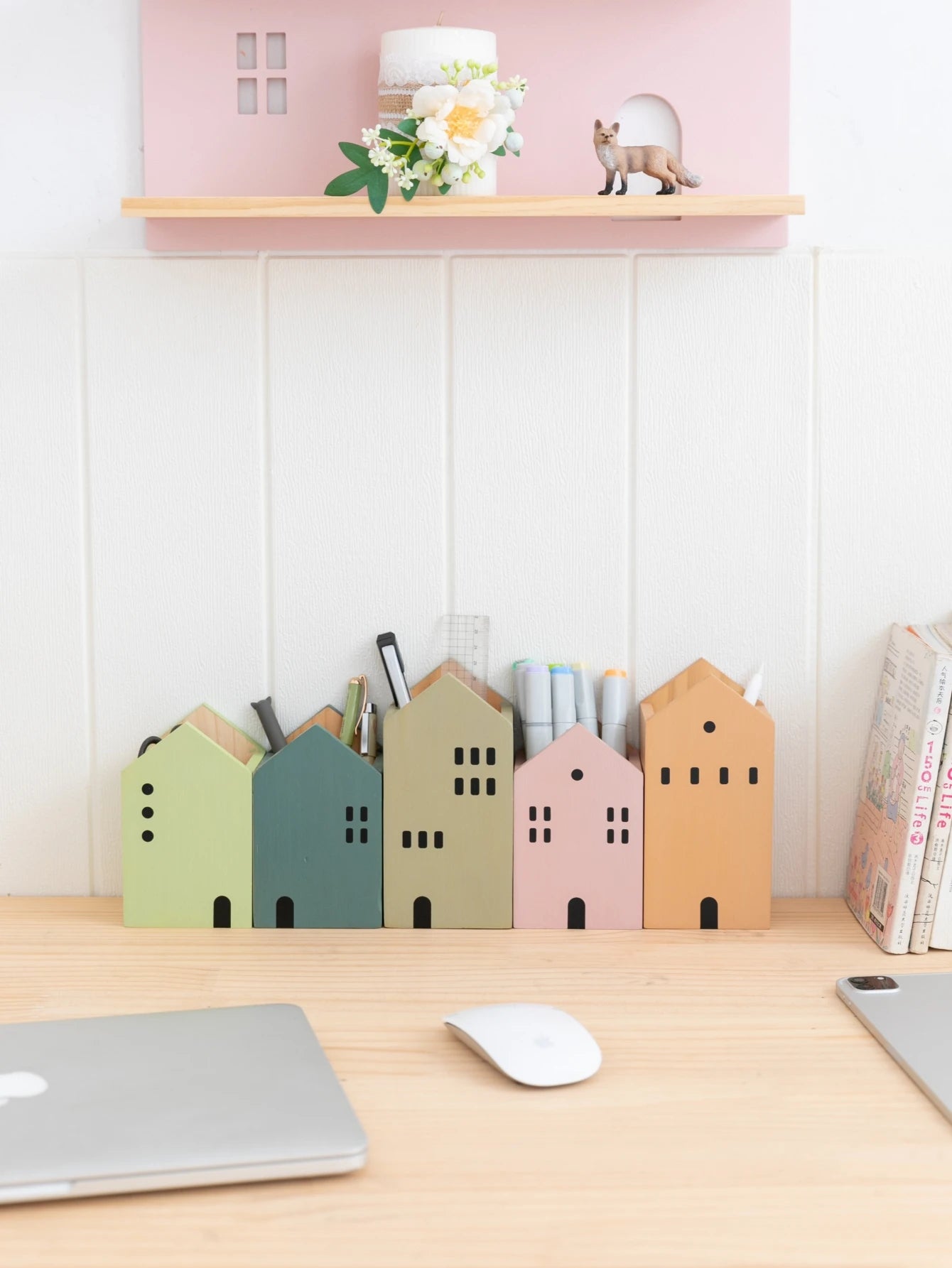Colorful house-shaped desk organizers on a wooden desk with a laptop and mouse.