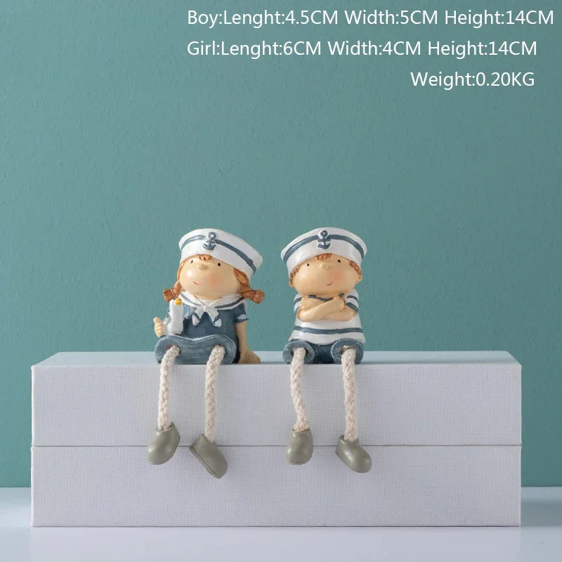 Two small figurines of a boy and girl in sailor outfits on a white box against a teal background.