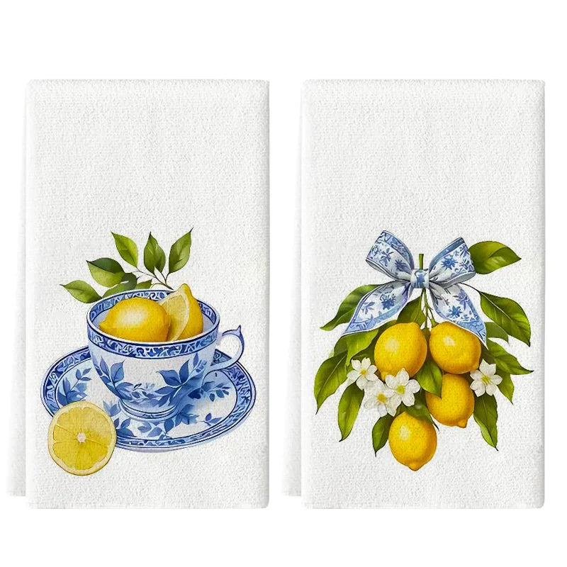 Two decorative towels with lemons and a teacup design on one, and lemons with a bow on the other, on a white background.