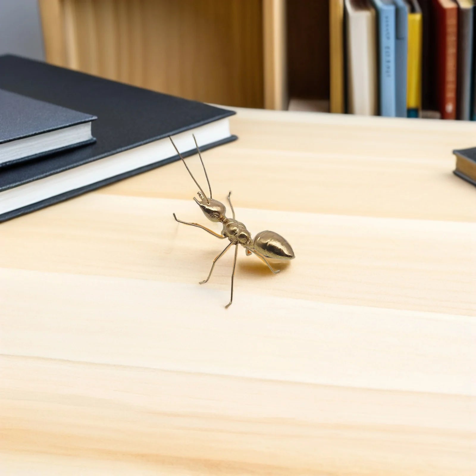 Metallic ant figurine on a wooden surface with books in the background
