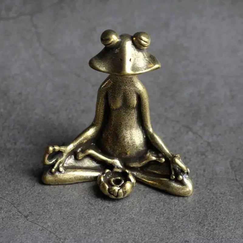 Bronze frog figurine in a meditative pose on a gray background