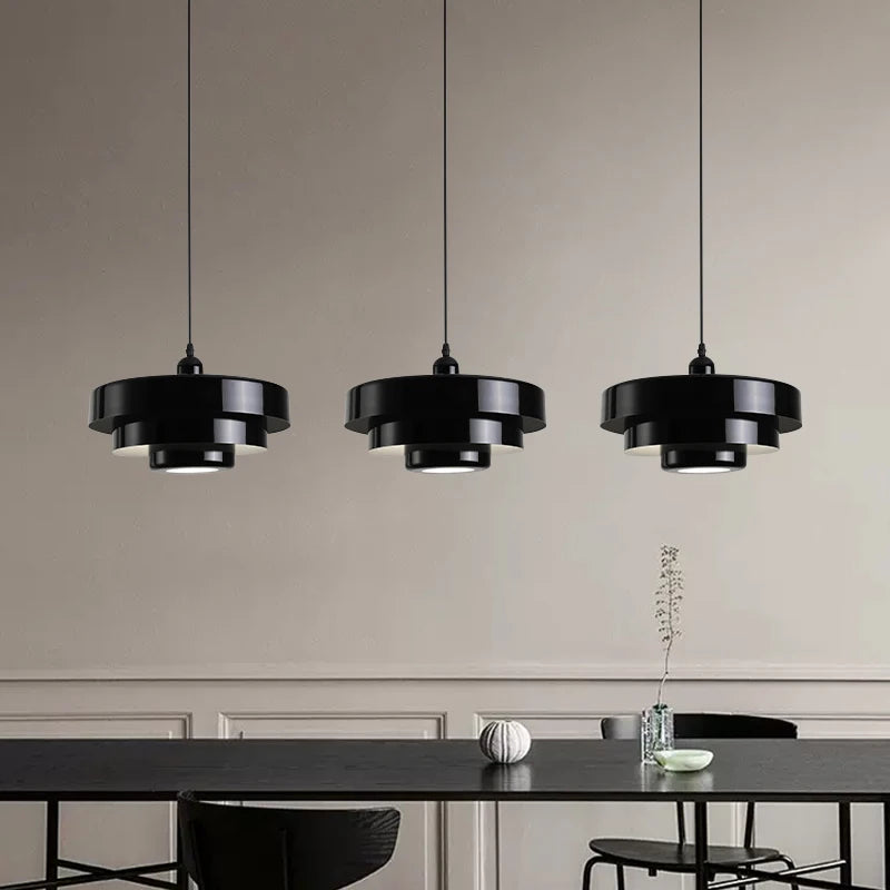 Three black pendant lights hanging above a dining table with a neutral wall background.