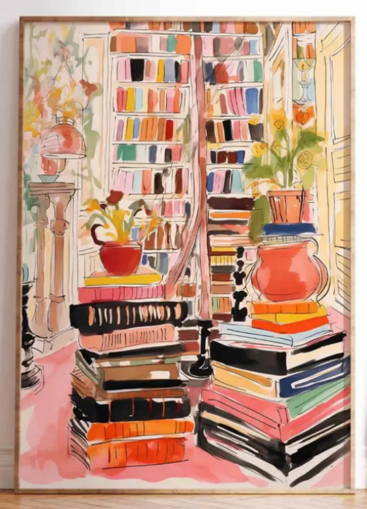 A framed watercolor painting depicting a cozy library scene with tall bookshelves, stacks of books, potted plants, and a pink floor, shown in a light wood frame.