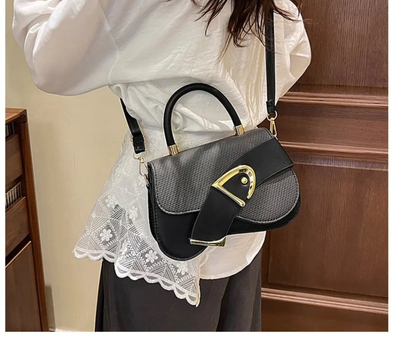 Person wearing a black and gray handbag with gold accents indoors.