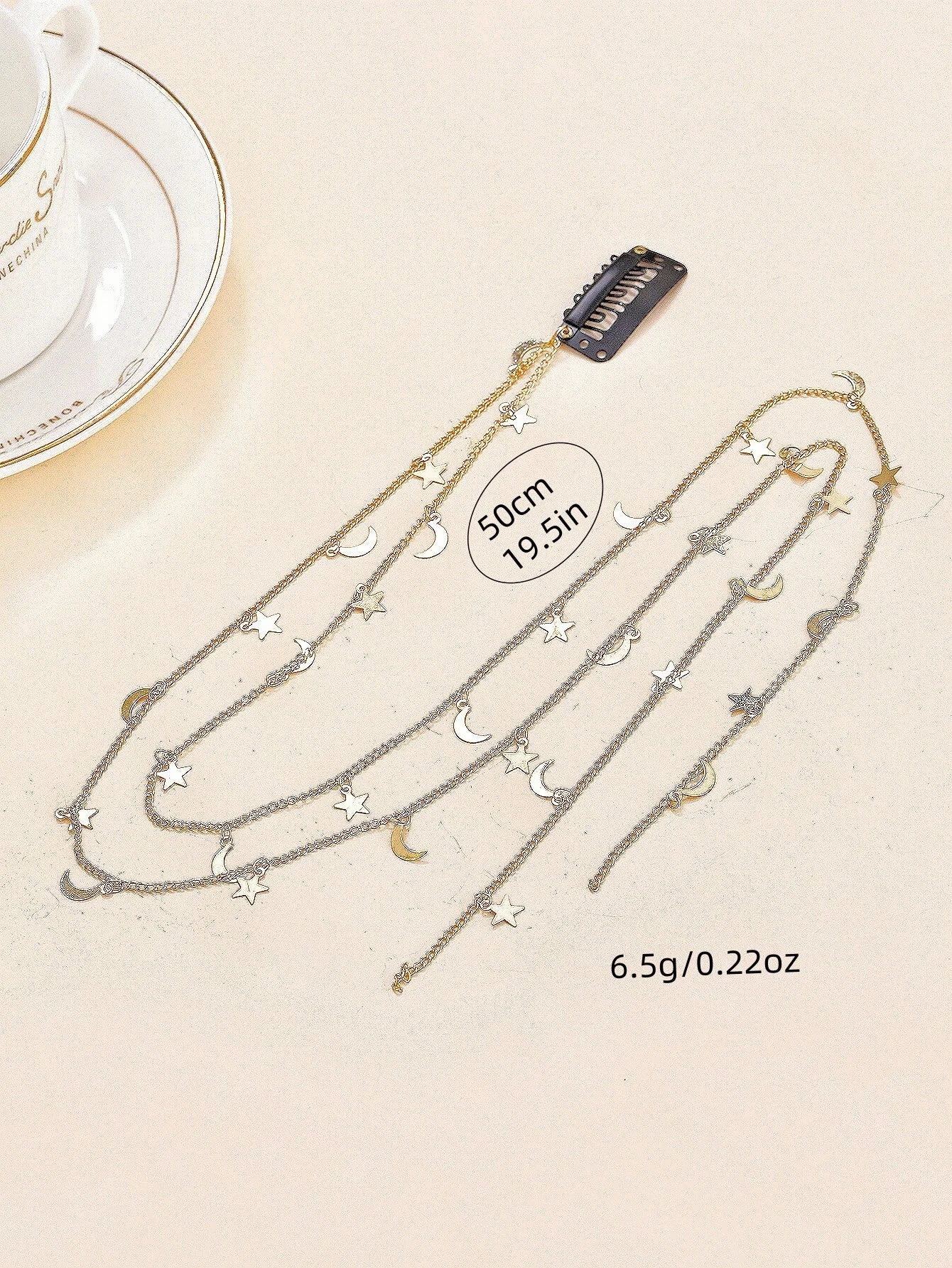 Necklace with star and moon pendants on a beige surface with a teacup in the background.