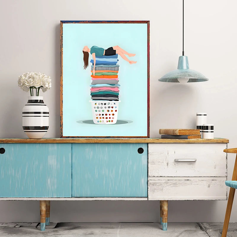 Framed artwork of a stack of clothes on a wooden shelf with decorative items.