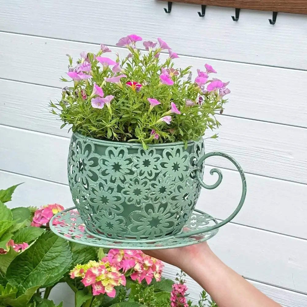 Decorative metal teacup planter with flowers on a white wooden background