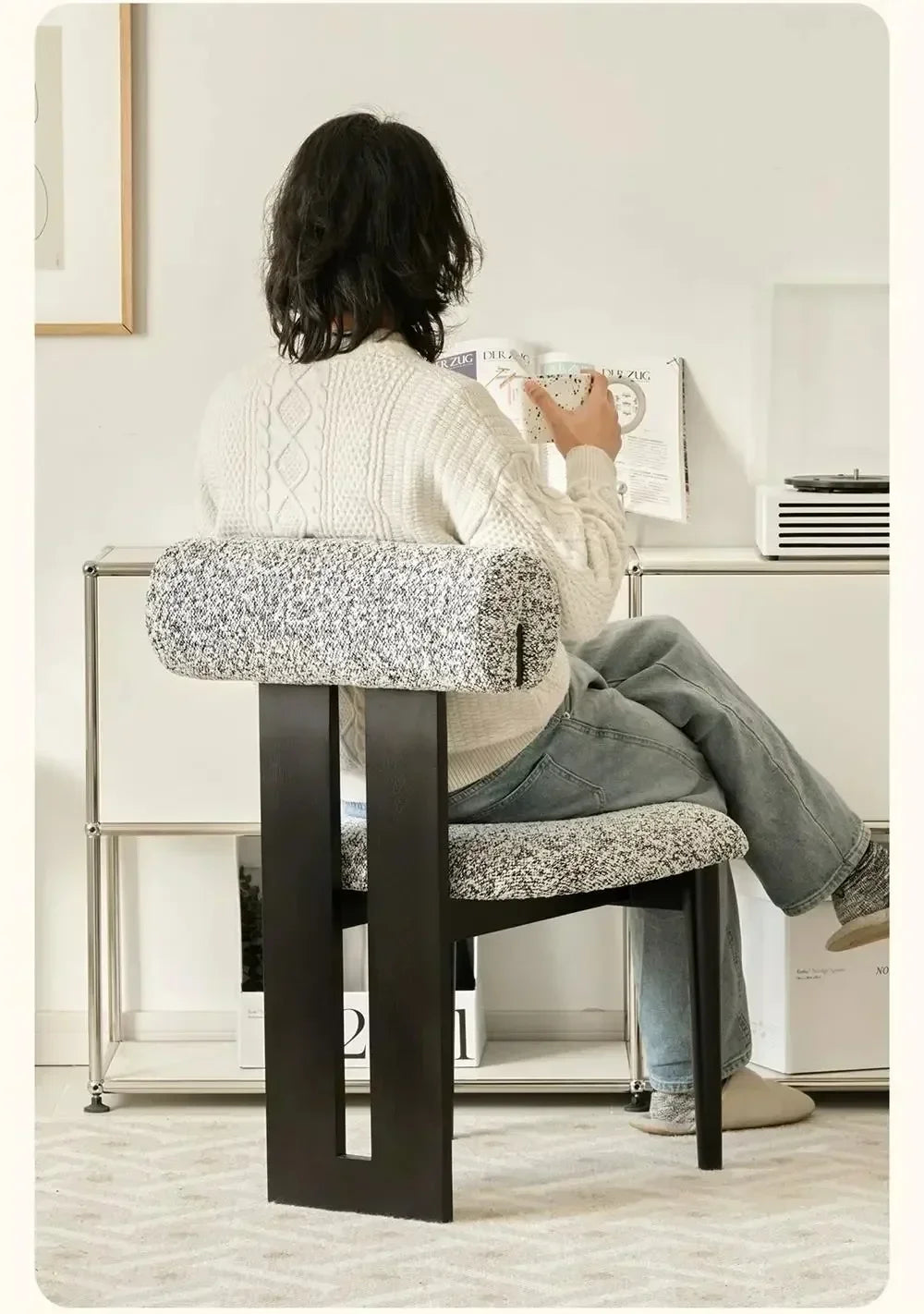 Person sitting on a modern chair reading a newspaper in a minimalistic room.